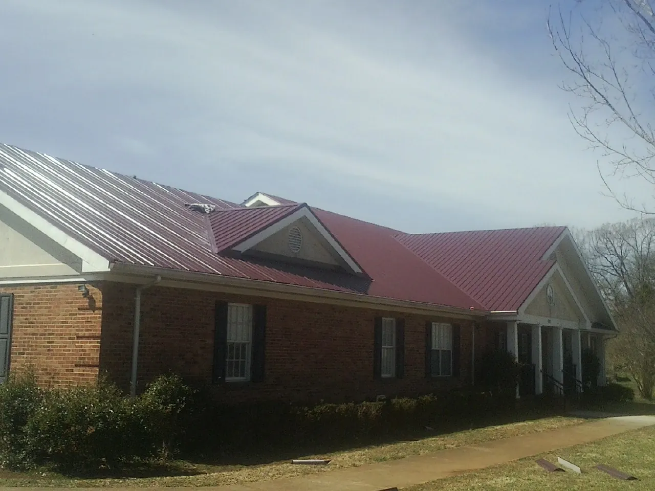 Red metal roof with gabled entries on a long brick building, from a Hail Damage Roof Repair job in Waverly