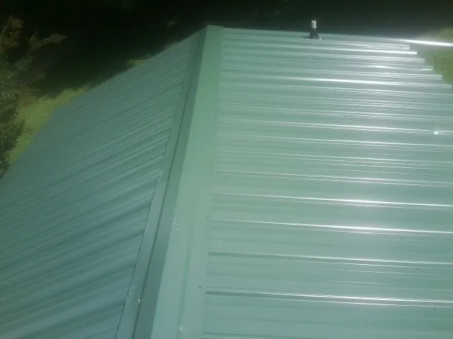 New green metal panels meeting at the ridge of a roof — Flat Roof Repair work by our crew in Waverly
